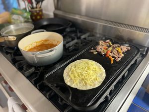 Quesadilla cooking in the foreground with pasta sauce heating up behind