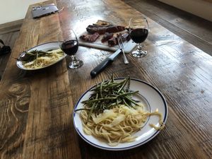 Plates with pasta and string beans, glasses of wine, and a cutting board with steak