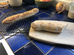 Two baguettes; one on a wire rack, the other cut in half on a cutting board