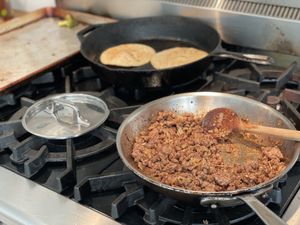 Taco meat in the pan, tortillas warming in the background