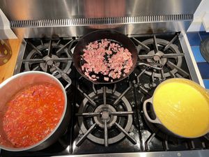Pots of polenta with tomato/beans cooking, and a pan of pancetta in the background