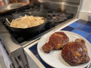 Steak resting while onions caramelize in the background